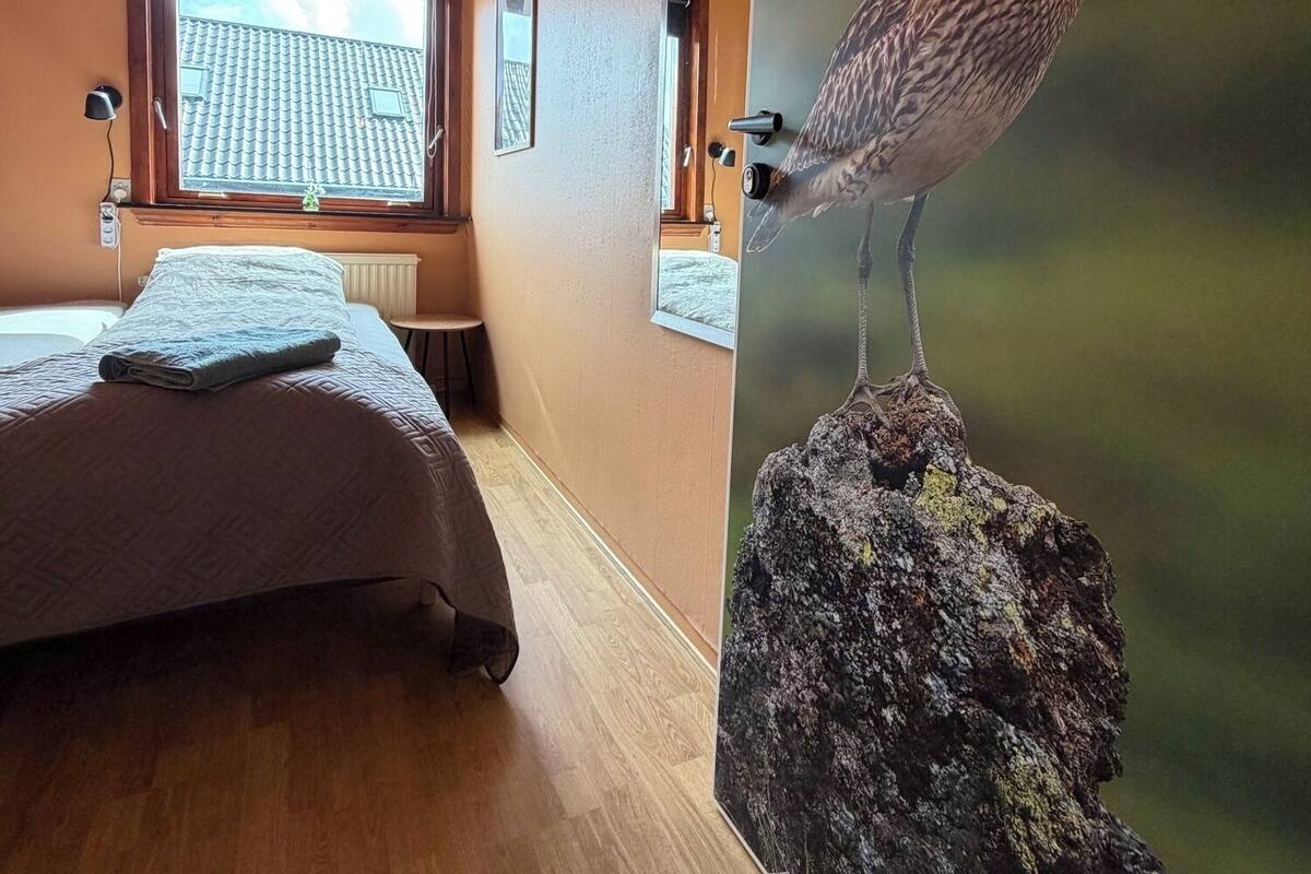 Un dormitorio con cama, ventana y un cuadro de un pájaro colgado en la pared.