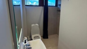 A modern bathroom with a white sink, a toilet, and a shower area. - Guesthouse Leon (Torshavn)