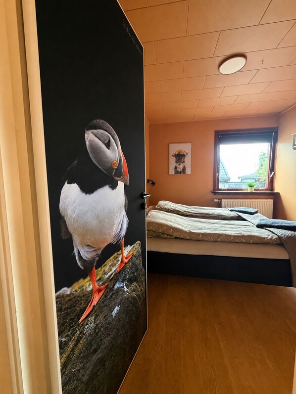 Una habitación con una cama, una ventana con vistas, una puerta con un cuadro de pez globo y una lámpara en el techo.