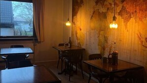 A restaurant interior with tables and chairs, a large map on the wall, and hanging pendant lights. - Guesthouse Leon (Torshavn)