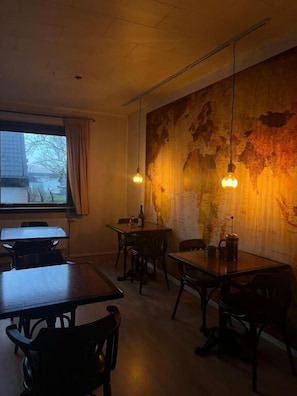 A restaurant interior with tables and chairs, a large map on the wall, and hanging pendant lights. - Guesthouse Leon (Torshavn)