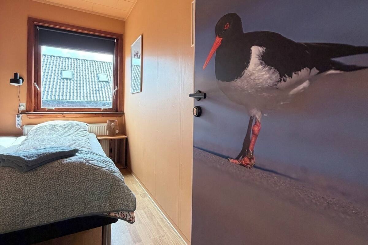 Una habitación con cama, ventana con vista a un tejado de tejas y una pared con un mural de aves.