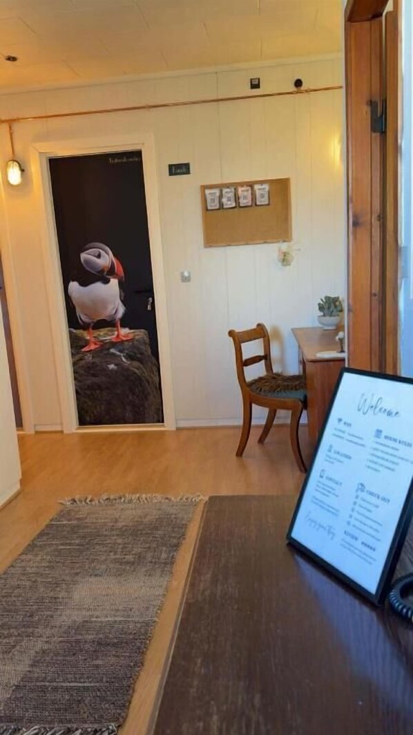 A hotel room with a wooden floor, a rug, a wooden chair, a small table, a bulletin board, and a menu stand.