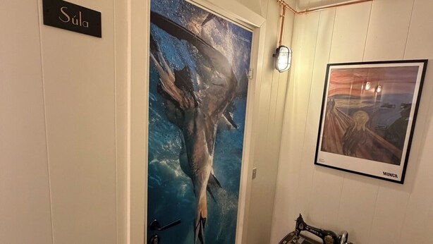 A room with a door labeled 'Súla,' a vintage sewing machine on a table, and a framed painting on the wall. - Guesthouse Leon (Torshavn)
