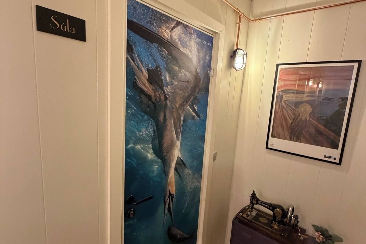 Una habitación con una puerta que dice 'Súla', una máquina de coser antigua sobre una mesa y un cuadro en la pared.