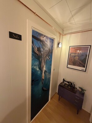 A room with a door labeled 'Súla,' a vintage sewing machine on a table, and a framed painting on the wall.