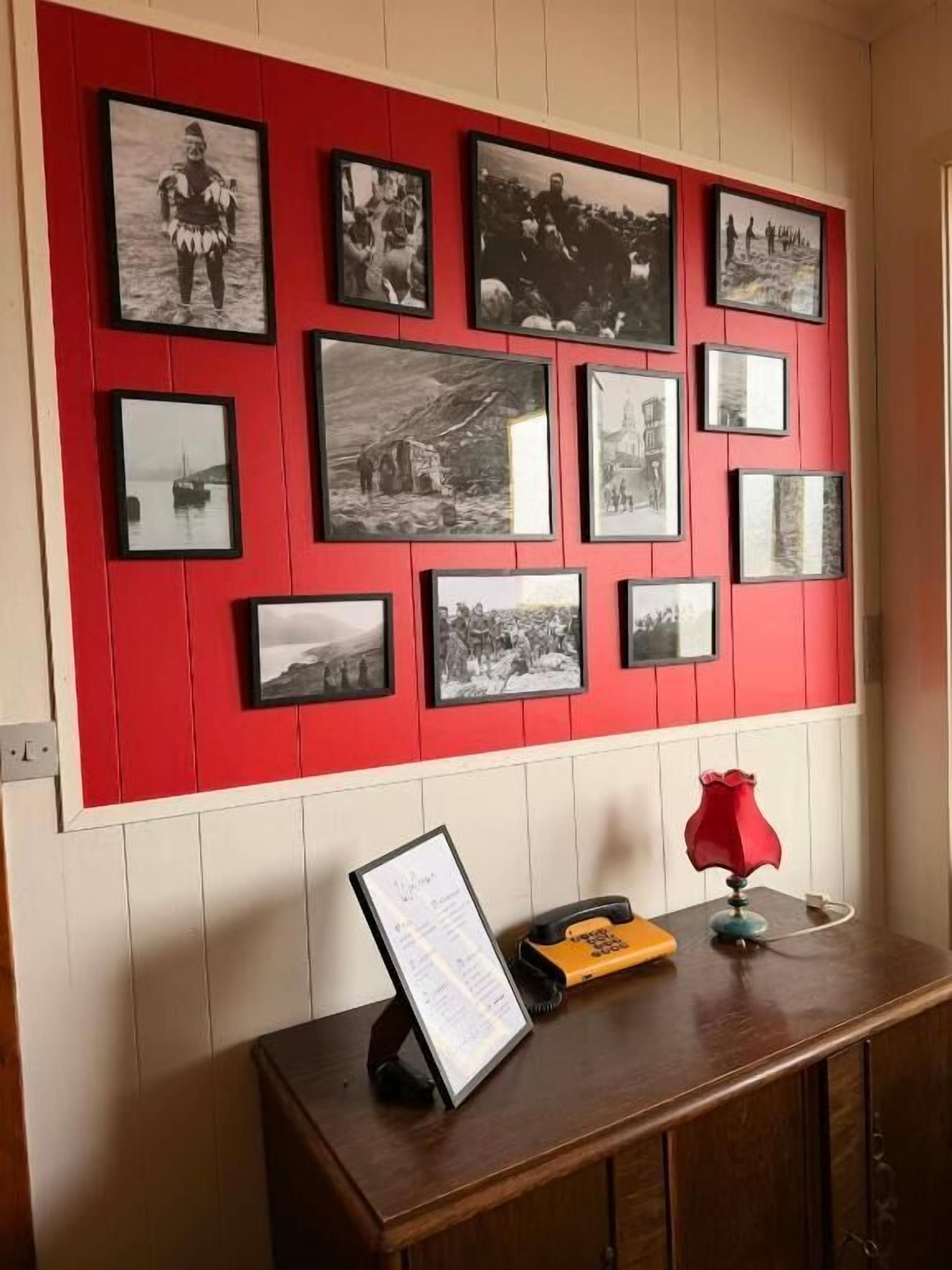 Una pared con varias fotografías en blanco y negro, una mesa de madera con un atril para el menú, y una lámpara roja.