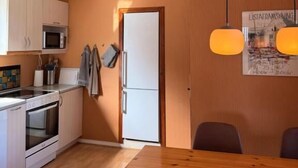 A compact kitchen with white appliances, a wooden dining table, and a hanging light fixture. - Guesthouse Leon (Torshavn)