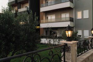 Un edificio moderno con balcones, un jardín y luminarias exteriores.
