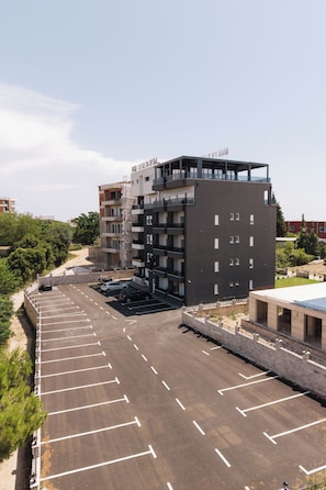 Una estructura de estacionamiento de varios pisos contigua a un edificio moderno con balcones y un cielo despejado.