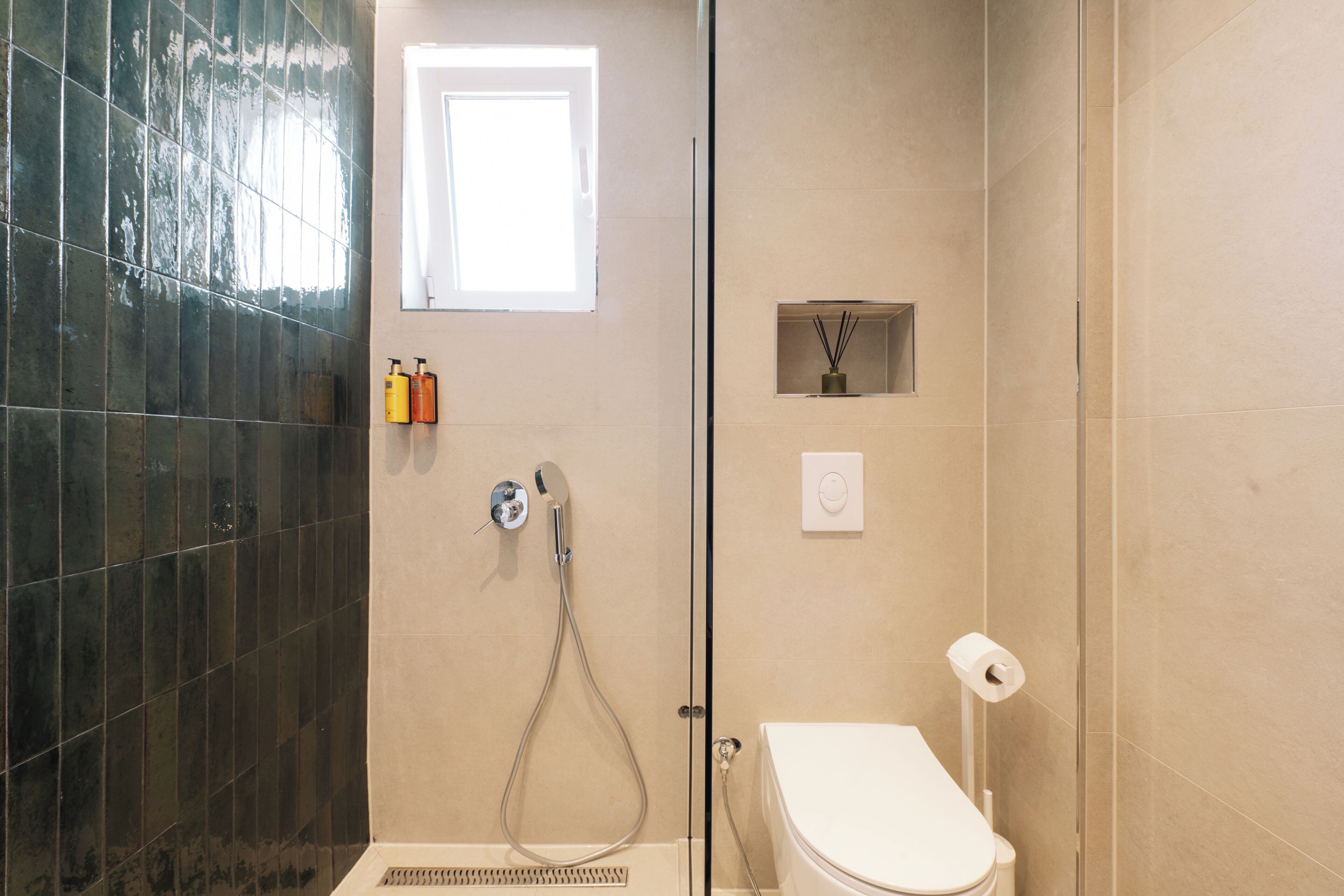 A bathroom with a shower, toilet, and a small window.