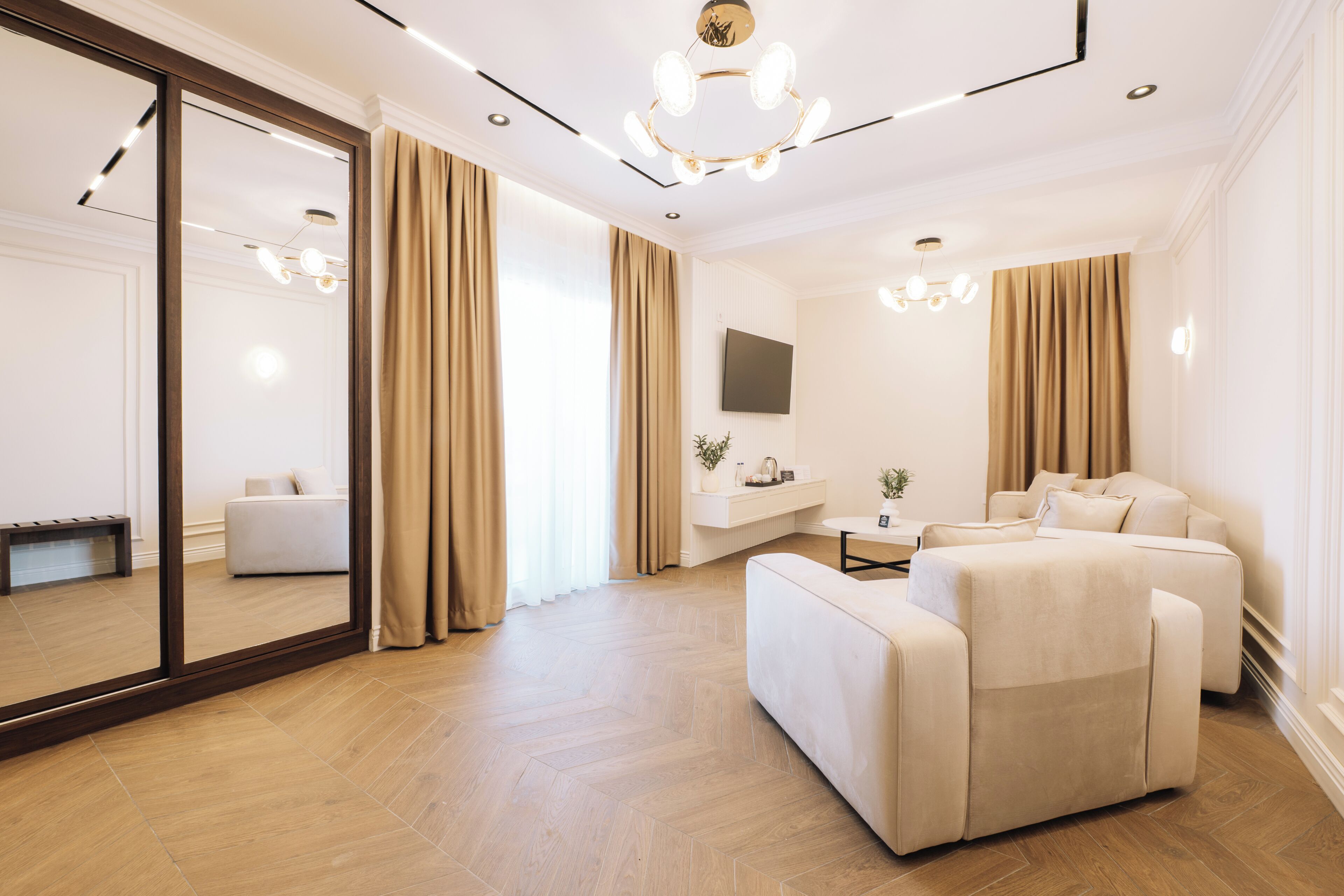 Une chambre d’hôtel moderne, dotée d’un grand miroir, d’un canapé, d’une télévision et d’un luminaire fixé au plafond.