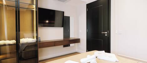 Habitación de hotel con cama, televisor montado en la pared, armario de madera y una puerta.