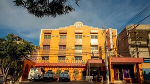A multi-story hotel with a yellow facade, a central entrance, and a parking area with several vehicles. - Hotel Santa María (Mazatlán)