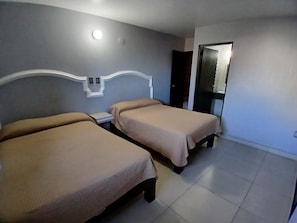 Hotellihuone, jossa on kaksi sänkyä, yöpöytä, peili ja ovi.
