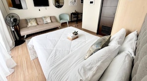 A neatly arranged bedroom with a bed, a sofa, a chair, a desk, and a television. - Modern Resort Stay Studio (Iloilo City)