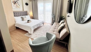 A bedroom with a bed, a sofa, a chair, a TV, and a window with curtains. - Modern Resort Stay Studio (Iloilo City)