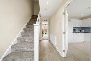 A staircase leading to a door, a kitchen with white cabinets and a blue backsplash, and a hallway with light-colored flooring. - Cosy 3 bed house in Aylesbury (Aylesbury)