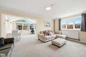 A spacious living area with a large window, a sofa set, a dining table, and a chair. - Charming house with Garden in Aylesbury (Aylesbury)