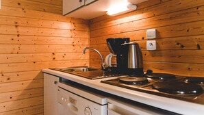 A kitchen with wooden walls, a stove, a sink, and a coffee maker. - Nature Cottage Near Puy du Fou (Moncoutant-sur-Sèvre)