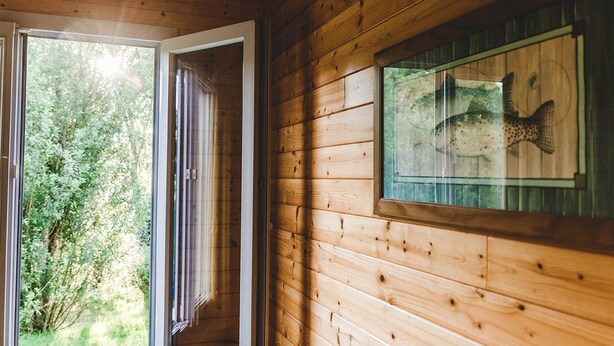 A wooden cabin interior with a glass fish display on the wall and a door leading to a garden. - Nature Cottage Near Puy du Fou (Moncoutant-sur-Sèvre)