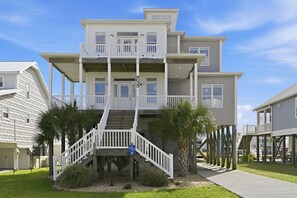 Ein mehrstöckiges Gebäude direkt am Strand mit einer zentralen Treppe, Balkonen und einer kleinen Gartenanlage.