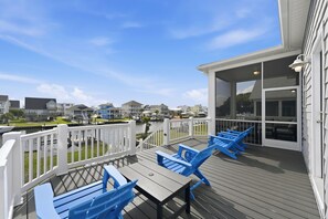 Eine Terrasse mit blauen Stühlen und einem Tisch, mit Blick auf ein Gewässer, im Hintergrund Häuser.
