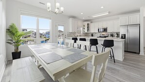 Een moderne keuken met witte kasten, een roestvrijstalen koelkast en een eethoek met een grote tafel en stoelen.