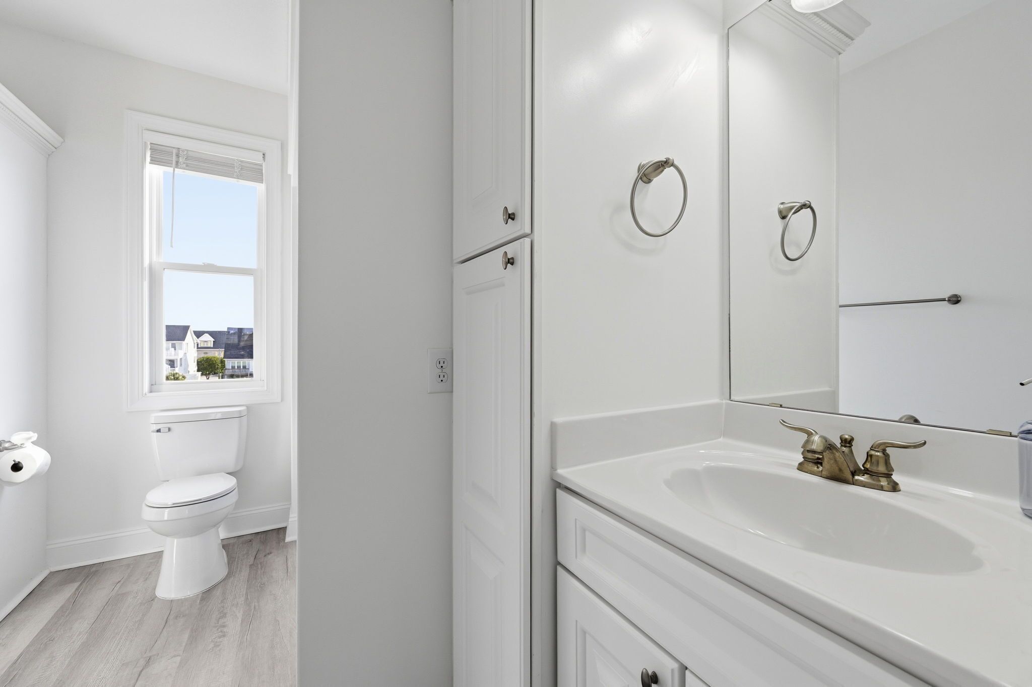 A bathroom with a toilet, sink, mirror, and window.