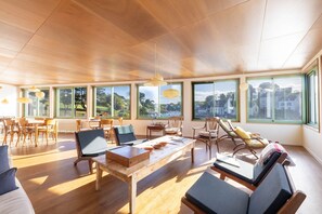 Ein geräumiges Zimmer mit einem Holztisch, Stühlen und Blick ins Freie durch große Fenster.