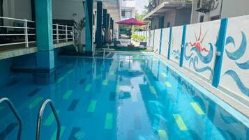 Piscina interior con agua azul cristalina, una escalera metálica y un mural en la pared.