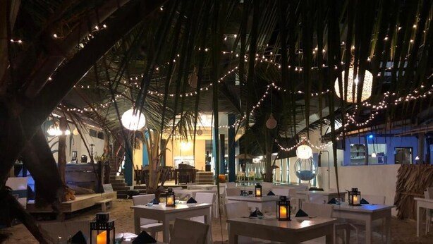 Un área de comedor al aire libre con mesas y sillas, luces colgantes y faroles.