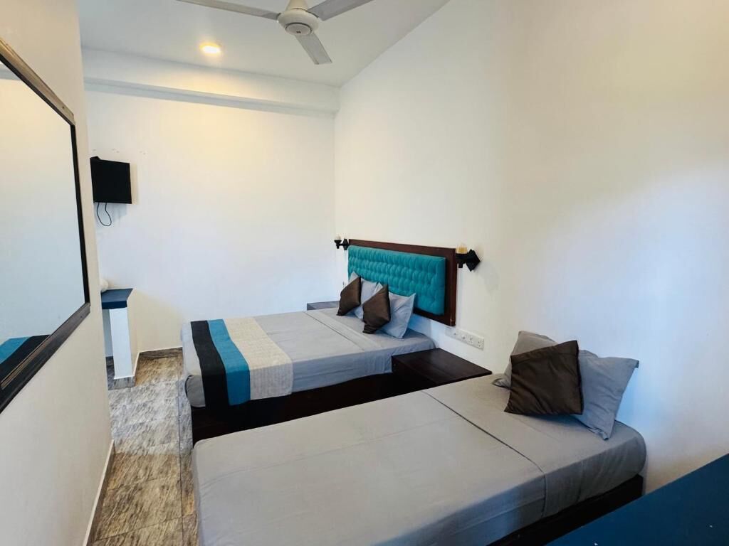 Une chambre avec deux lits, un ventilateur de plafond, un téléviseur fixé au mur et une petite table.