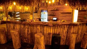 Una zona con barra de madera, techo de paja, un menú digital y taburetes.