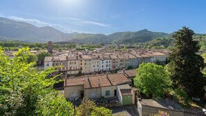 Uma cidade com edifícios tradicionais, uma torre do relógio imponente e montanhas ao fundo.