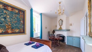 Um quarto com cama, lareira, mesa de jantar e um grande quadro floral.