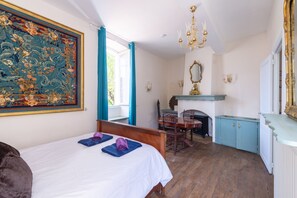 Ein Zimmer mit einem Bett, einem Kamin, einem Esstisch und einem großen Blumenbild.