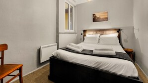 A bedroom with a bed, a chair, a radiator, a window, and a painting on the wall. - L'Halo Gloire - Charmant T2 de caractère (Toulouse)