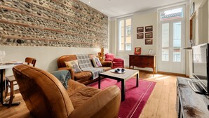 A living room with a stone wall, leather furniture, a television, and a dining area. - L'Halo Gloire - Charmant T2 de caractère (Toulouse)
