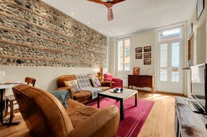 Una sala de estar con pared de piedra, muebles de cuero, televisor y comedor.