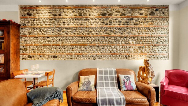 A living room with a stone wall, leather furniture, and a table with wine glasses. - L'Halo Gloire - Charmant T2 de caractère (Toulouse)
