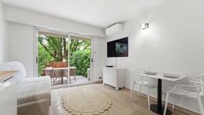 Un soggiorno moderno con un divano, un tavolo da pranzo con sedie, una TV a parete e una porta vetrata scorrevole che dà su una zona esterna con tavolo e sedie.