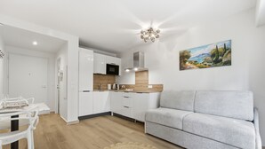 Una cucina moderna con mobili bianchi, un divano grigio e un quadro raffigurante un paesaggio.