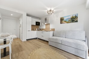 Eine moderne Küche mit weißen Schränken, einem grauen Sofa und einem Landschaftsbild.