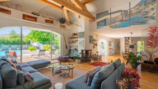 Ein großzügiger Wohnbereich mit einer großen Couch, einem Couchtisch und einem Kamin. Ein Balkon mit Pool und Gartenmöbeln ist vorhanden.