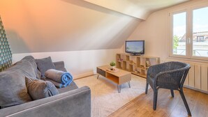 Una sala moderna con un sofá, una mesa de centro, un sillón de mimbre, un televisor y una ventana con vistas.