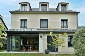 Ein zweistöckiges Haus mit überdachter Terrasse, großen Fenstern und einem gepflegten Garten.
