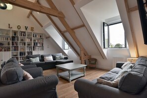 Ein Loft-Wohnzimmer mit schrägem Dach, einem Bücherregal, einem Sofa, einem Couchtisch und einem Fenster.