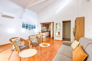 Ein Wohnzimmer mit einer Couch, zwei Korbstühlen, einem kleinen runden Tisch und einer Küche im Hintergrund.