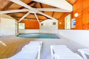Ein Innenpool mit weißen Liegestühlen, Holzbalkendecke und gefliestem Boden.